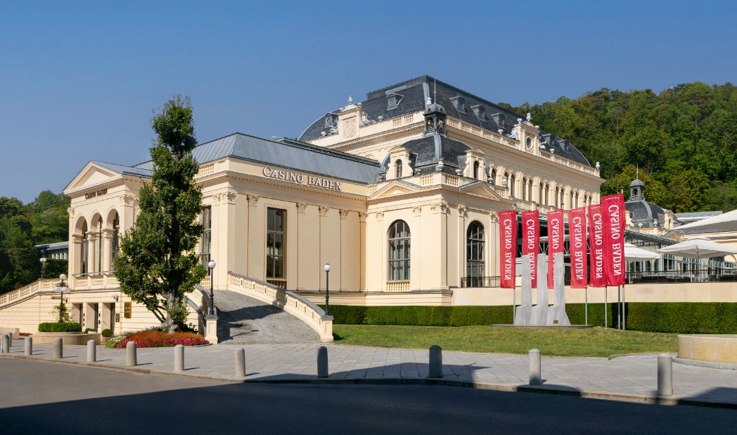 Casino Baden bei Wien im historischen Kurhaus bei Nacht mit elegant beleuchteter Fassade, Gästen in Abendkleidung und Hinweisschild zum Spielcasino – stilvolles Casinoerlebnis in Niederösterreich