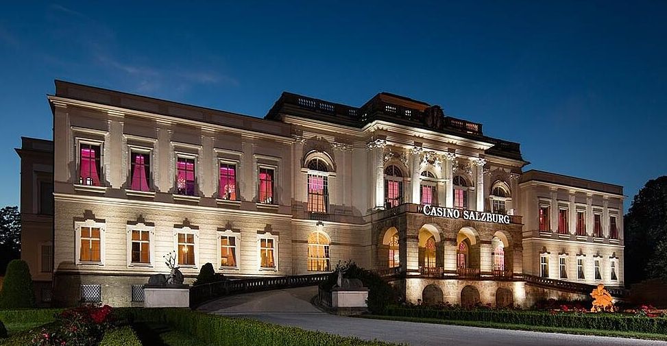 Casino Salzburg im barocken Schloss Klessheim bei Nacht mit elegant beleuchteter Fassade, Gästen in Abendgarderobe und Hinweisschild zum Spielcasino – Premium-Casinoerlebnis in Österreich